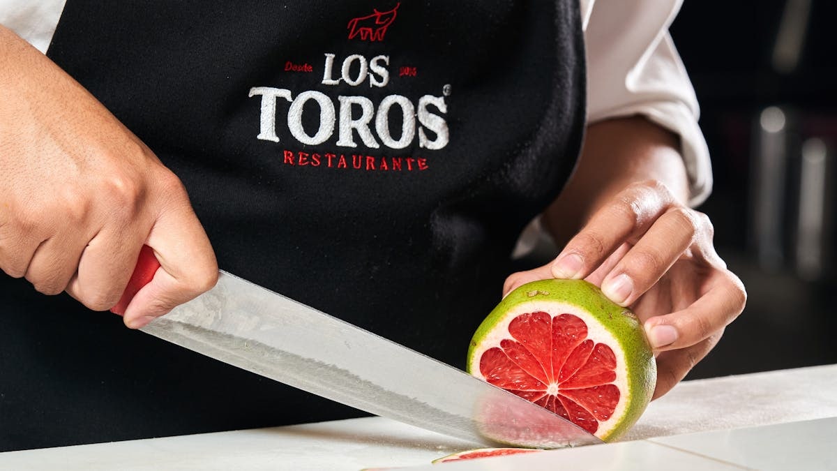 Close-up of chef slicing grapefruit wearing Los Toros Restaurant apron.