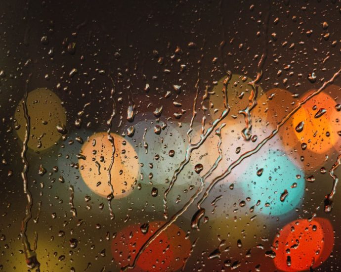 Close-up of raindrops on glass with blurred colorful city lights in the background.