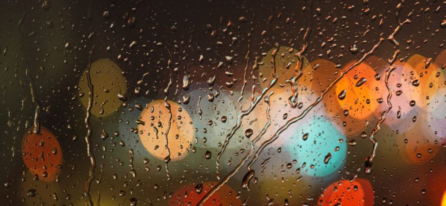 Close-up of raindrops on glass with blurred colorful city lights in the background.