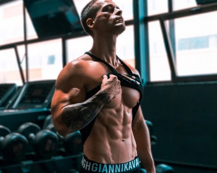 Muscular man showing abs and tattoos in a gym setting.